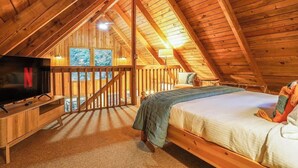 Een gezellig zolderkamer met houten plafond, een bed, een televisie en een raam met uitzicht op een besneeuwd landschap.