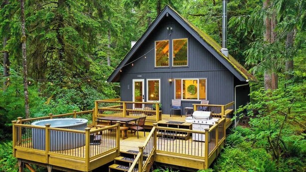 Een chalet met terras, hottub en een zitgedeelte buiten, omringd door bos.