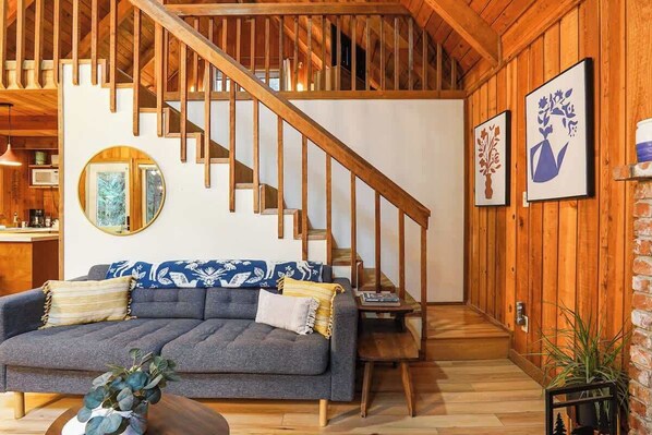 A wooden interior with a staircase, a gray sofa, and framed artwork on the walls.
