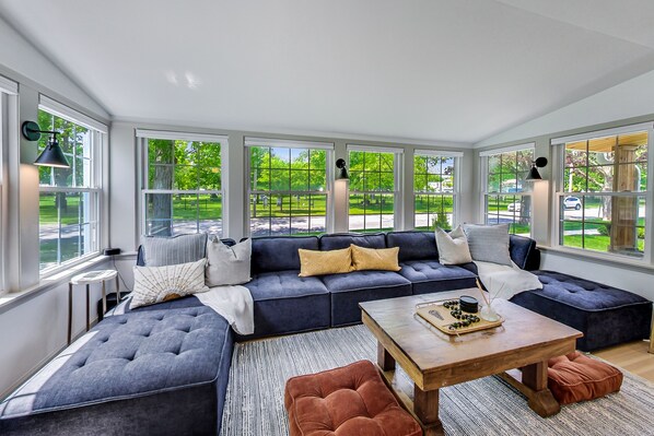 Relax on a large sectional sofa with ample seating and enjoy the view of a lush green park from the large windows.