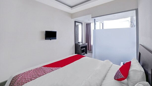 A hotel room with a bed, a TV, a mirror, and a door leading to a bathroom. - Hotel O Wesly House (Medan)