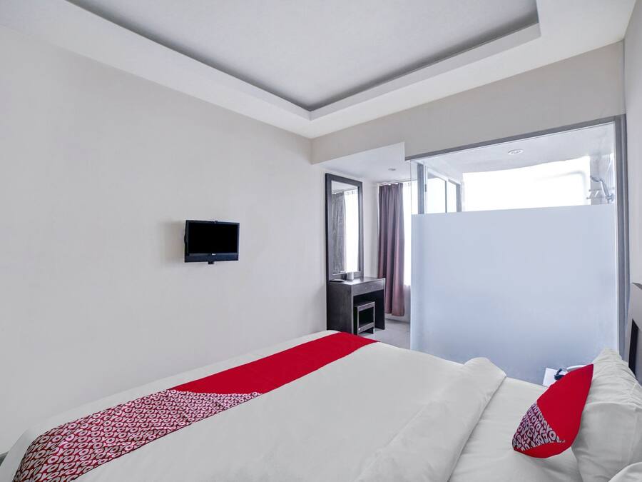 A hotel room with a bed, a TV, a mirror, and a door leading to a bathroom.