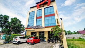 A building with a large sign, multiple windows, and parked cars in front. - Hotel O Wesly House (Medan)