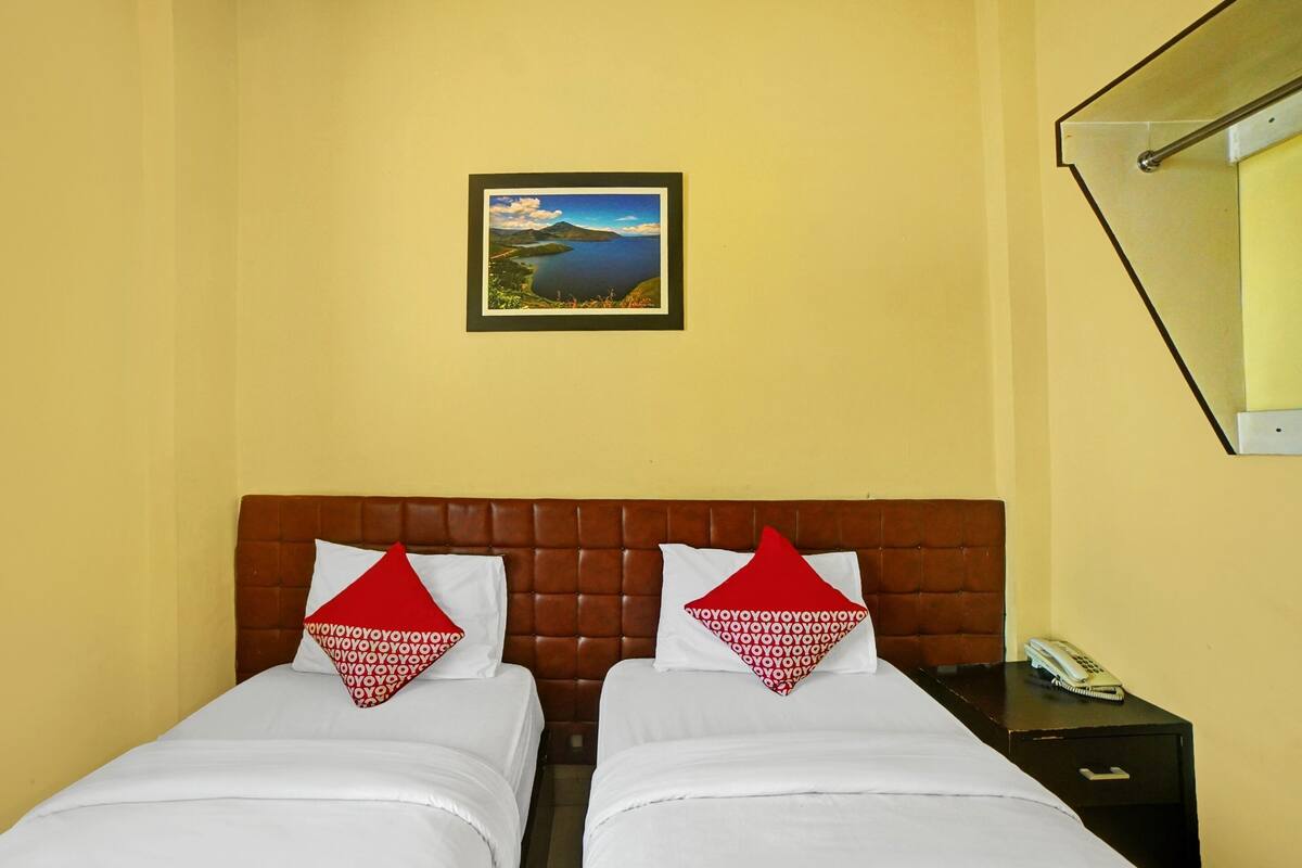 Camera d'albergo con due letti, un poggiatesta marrone, un quadro incorniciato raffigurante un paesaggio e un comodino con un telefono.