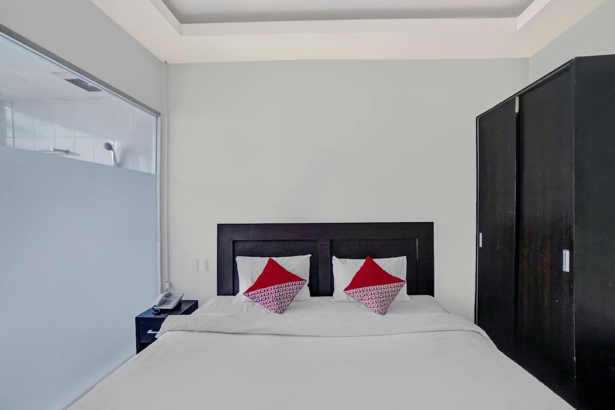 Una camera d'albergo con un letto grande, due cuscini, un comodino con il telefono e un armadio.