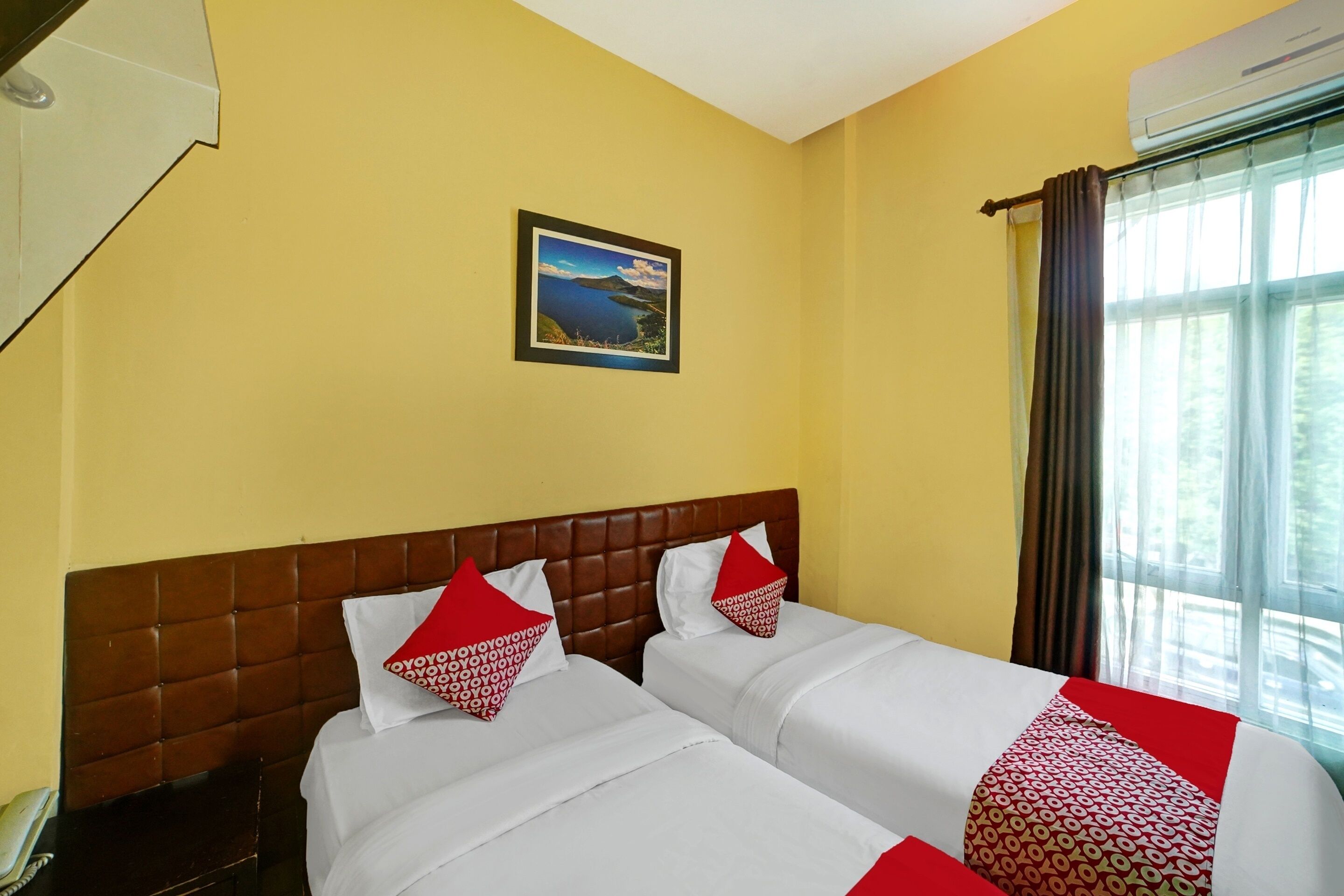 A hotel room with two beds, a brown headboard, a framed picture on the wall, and a window with curtains.