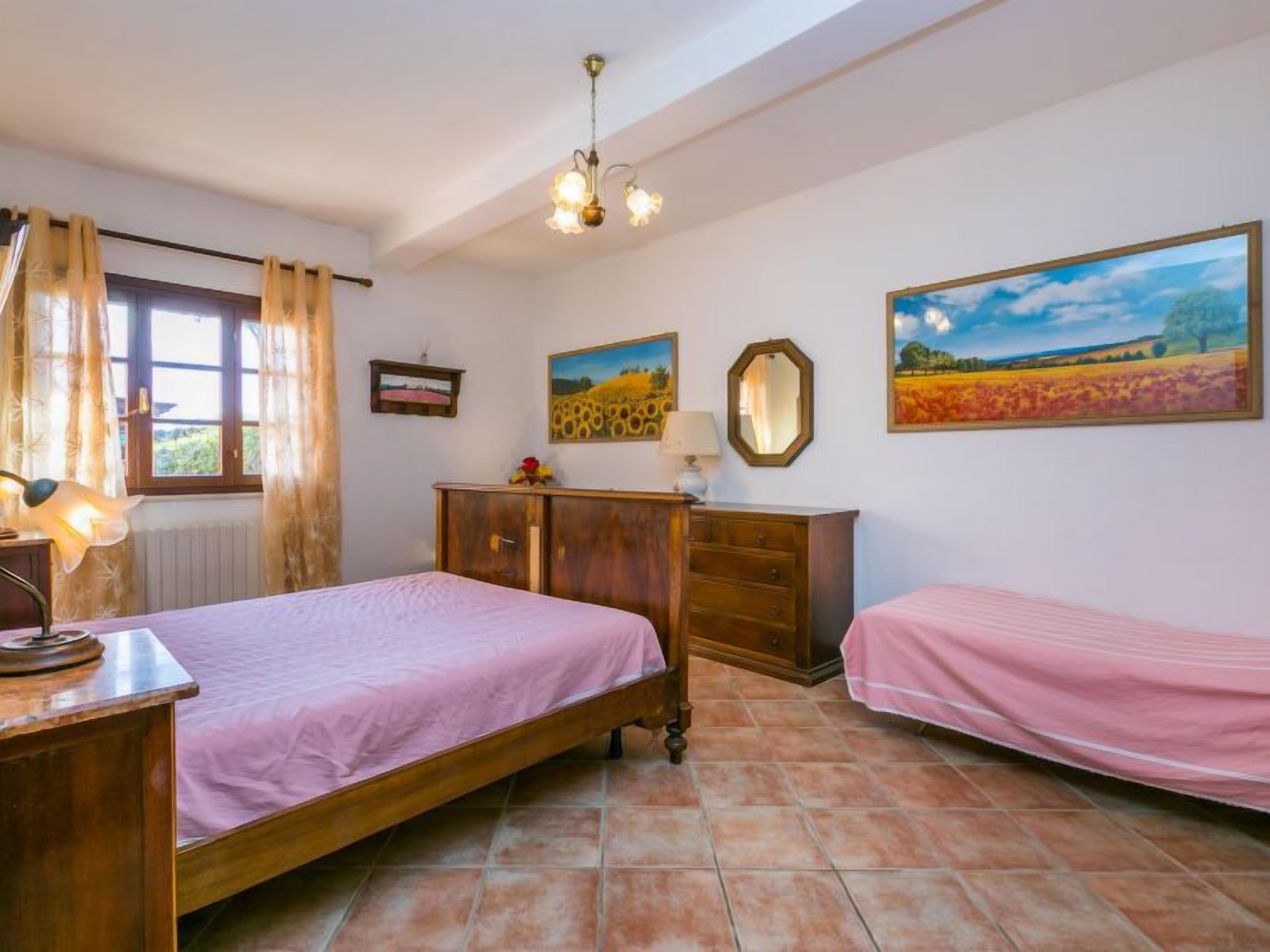 Een slaapkamer met twee bedden, een houten dressoir, een bureau, een lamp en twee schilderijen aan de muur.