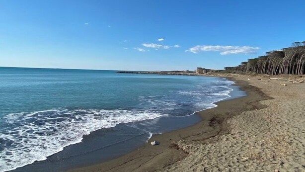 A beach with clear blue water, sandy shore, and a distant rocky outcrop. - La Casina by Interhome (Cecina)