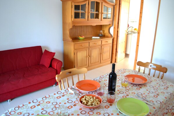 Un comedor con una mesa dispuesta para dos, un sofá rojo, armarios de madera y una ventana con luz natural.