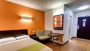 A hotel room with a bed, a desk, a chair, and a mirror.