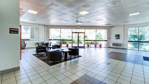A spacious indoor area with a tiled floor, several chairs and tables, a vending machine, and large windows offering a view of the outdoors.