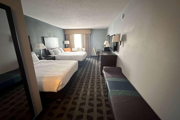 A hotel room with two beds, a desk, a TV, and a sofa.