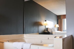 Un baño moderno con un espejo grande, una bañera, un lavabo y una mesita de noche con lámpara.