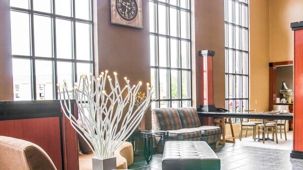 A lobby with seating, a clock, and large windows. - Baymont by Wyndham Flint Airport North (Flint)