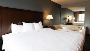 A hotel room with a large bed, a nightstand with a lamp, a mirror, and a bathroom with a sink and mirror. - Baymont by Wyndham Flint Airport North (Flint)