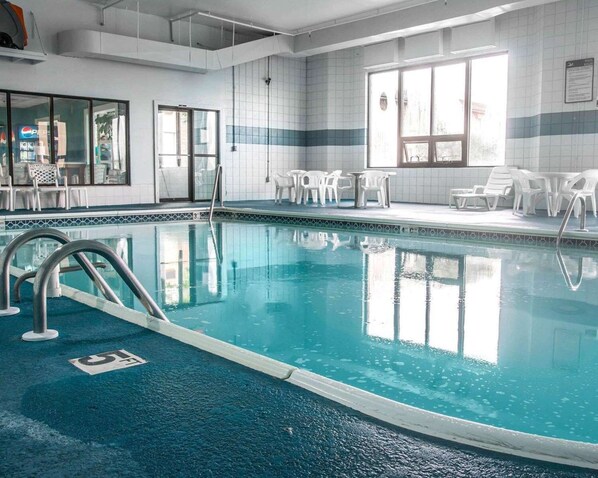 A swimming pool with clear blue water, surrounded by white chairs and tables, and a tiled wall with a window.