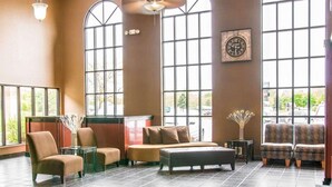 A spacious lobby with large windows, a clock on the wall, and a seating area with chairs and a sofa. - Baymont by Wyndham Flint Airport North (Flint)