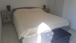 Ein Schlafzimmer mit einem Bett, zwei Nachttischen, einer Nachttischlampe und einem kleinen Hocker.