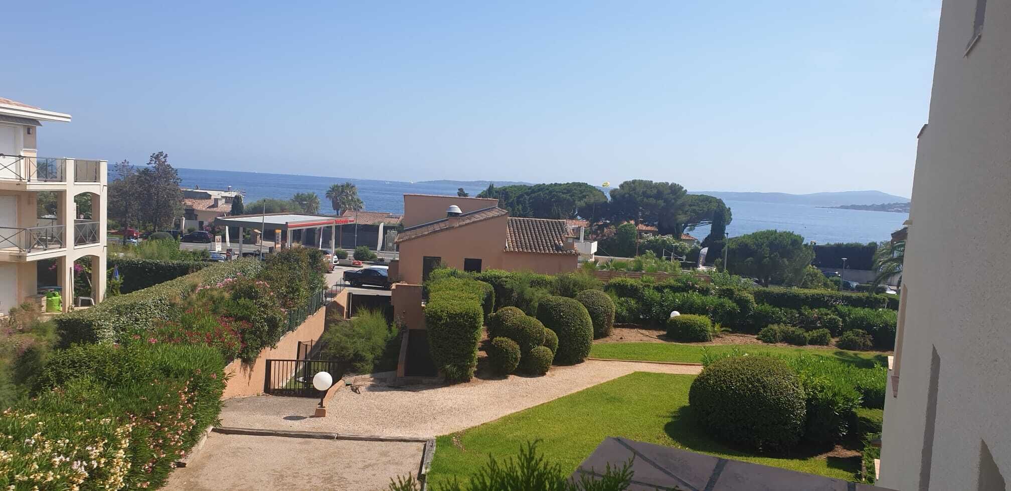 A residential area with a view of the sea, featuring a house with a garden and a paved pathway.