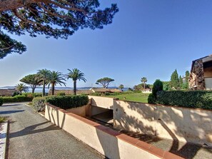 A coastal property with a paved driveway, a stone retaining wall, and a view of the sea and mountains in the background.