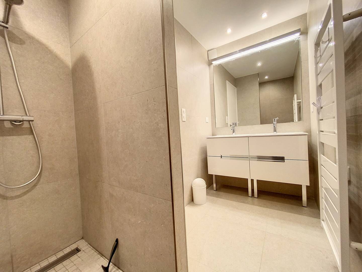 A modern bathroom with a walk-in shower, a large mirror, and a white vanity with a sink.