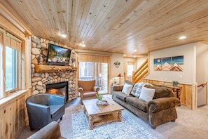 A cozy living room with a stone fireplace, a television mounted on the wall, and a comfortable seating area with a sofa and chairs.