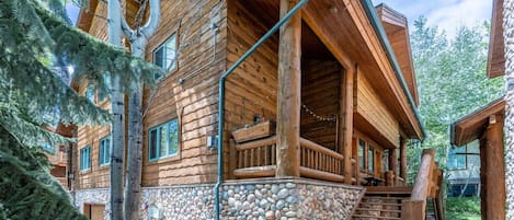 Una cabaña de madera con base de piedra, un porche y una escalera que lleva a la entrada.
