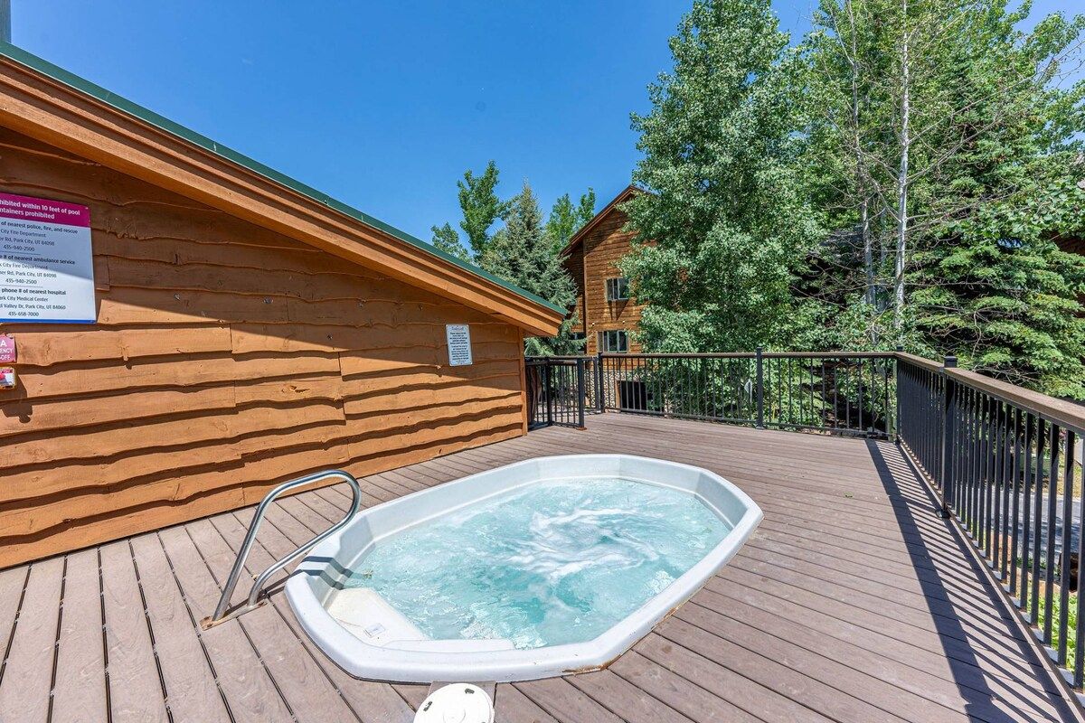 Una cabaña de madera con un jacuzzi en una terraza, rodeada de árboles.