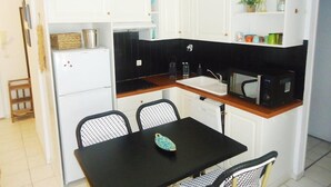 A compact kitchen with white cabinets, a black countertop, a white sink, a microwave, and a small dining table with two chairs. - Bel Appartement 3 Pièces Climatisé 400m des Plages (CAVALAIRE SUR MER)