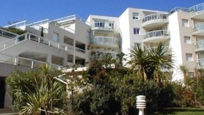 A multi-story hotel with balconies, surrounded by greenery and palm trees. - Bel Appartement 3 Pièces Climatisé 400m des Plages (CAVALAIRE SUR MER)