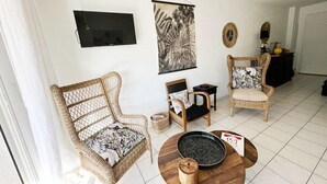 A living room with wicker furniture, a flat-screen TV, a large plant, and a round coffee table. - Bel Appartement 3 Pièces Climatisé 400m des Plages (CAVALAIRE SUR MER)