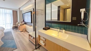A modern hotel room with a large bed, a desk, a chair, a TV, a bathroom with a large mirror, and a shower.