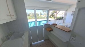 A compact kitchen with a window overlooking a balcony, a sink, and a countertop with a towel. - Studio for 2 people in the heart of Saint-Tropez (ST TROPEZ)