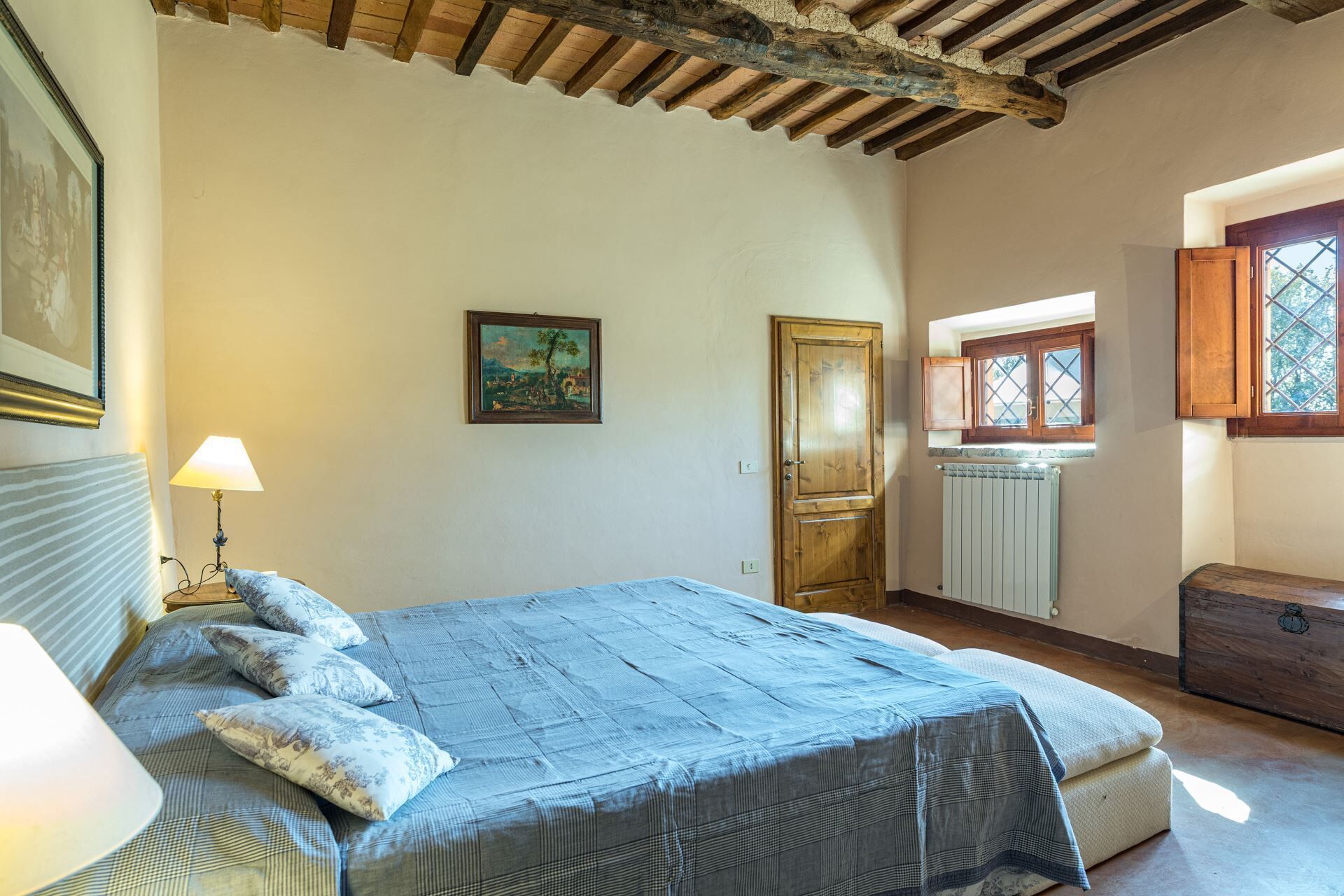 Ein Schlafzimmer mit Bett, Nachttisch, Lampe, Holztür, Fenster und Heizkörper.