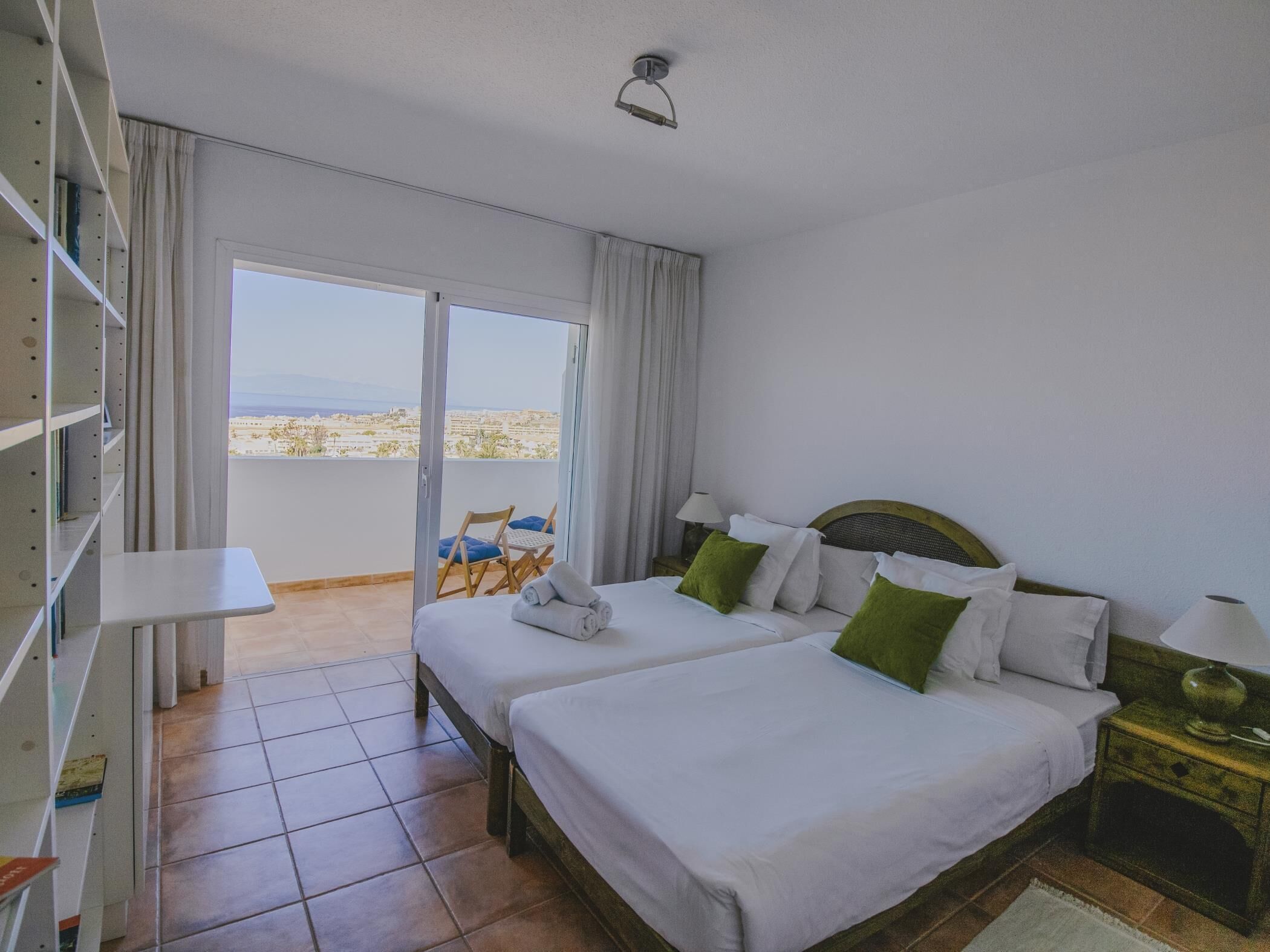 A hotel room with two beds, a balcony with a view, and a small table.