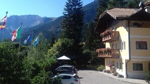 A building with a traditional Alpine architectural style, a parking area, and a mountainous backdrop. - Majon Fior de Bosch 1 (Campitello di Fassa)