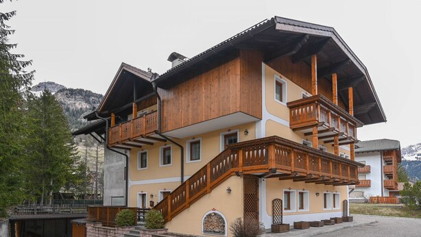 A multi-story chalet with wooden balconies, a stone staircase, and a mountain backdrop. - Majon Fior de Bosch 1 (Campitello di Fassa)