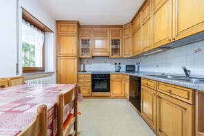 Una cocina con armarios de madera, microondas, lavamanos y una mesa con mantel rojo y blanco.