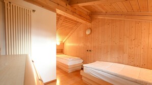 En stuga med träpanel, två sängar, ett vitt element och ett trätak.