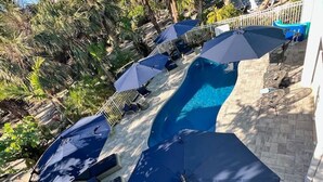 Ein Poolbereich mit mehreren Sonnenschirmen und Liegestühlen, umgeben von Palmen.