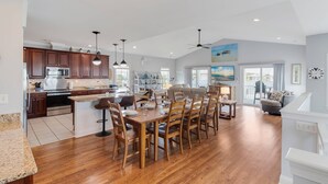 A spacious kitchen with wooden cabinets, a dining area with a large wooden table, and a view of the outside. - Amazing Home with Pool, Golf Cart, Elevator, Hot Tub, Fire Pit Short Walk to the Beach (Oak Island)