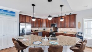 A modern kitchen with granite countertops, stainless steel appliances, and brown wooden cabinets. - Amazing Home with Pool, Golf Cart, Elevator, Hot Tub, Fire Pit Short Walk to the Beach (Oak Island)