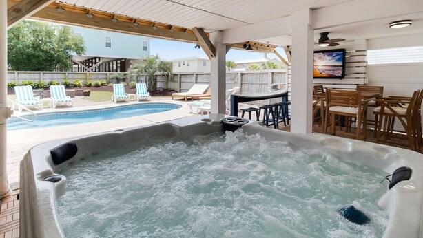 A hot tub with a wooden deck and outdoor furniture, a pool, and a view of neighboring houses. - Amazing Home with Pool, Golf Cart, Elevator, Hot Tub, Fire Pit Short Walk to the Beach (Oak Island)