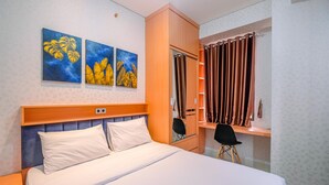 A hotel room with a bed, a wardrobe, a desk, and two paintings on the wall.