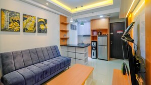 A modern living room with a sofa, a wooden coffee table, and a kitchen area with cabinets and appliances.