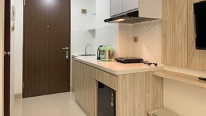 A modern kitchen with a wooden door, white tiled backsplash, and a built-in microwave. - Elegant Studio At Transpark Cibubur Apartment Near Shopping Mall (Bekasi)