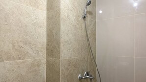 A bathroom with a shower, toilet, and a roll of toilet paper on the floor. - Elegant Studio At Transpark Cibubur Apartment Near Shopping Mall (Bekasi)