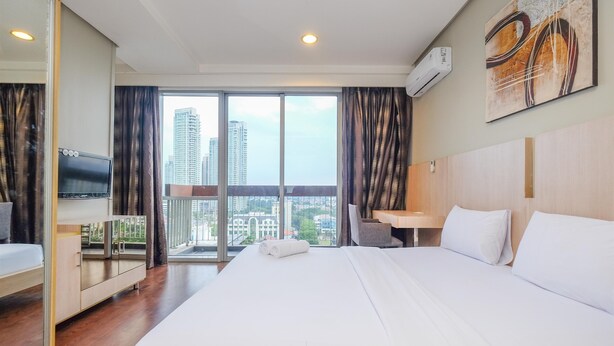 A hotel room with a large bed, a desk, a TV, and a balcony with a city view.