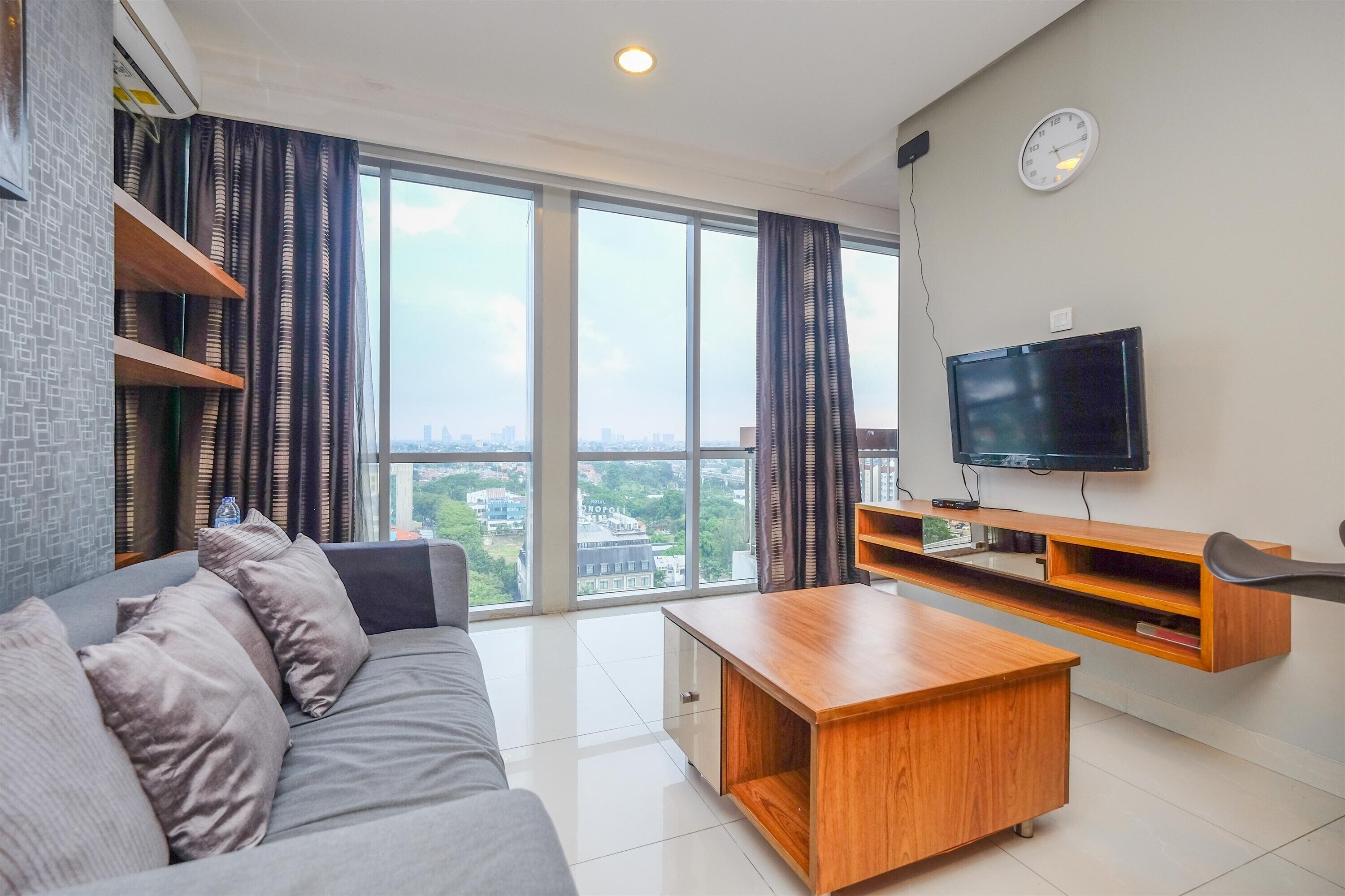 Una sala de estar moderna con sofá, mesa de centro, televisor y ventanas amplias que ofrecen vistas a la ciudad.