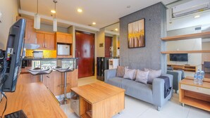 A modern living room with a grey sofa, wooden coffee table, and a kitchen area with wooden cabinets and a refrigerator.